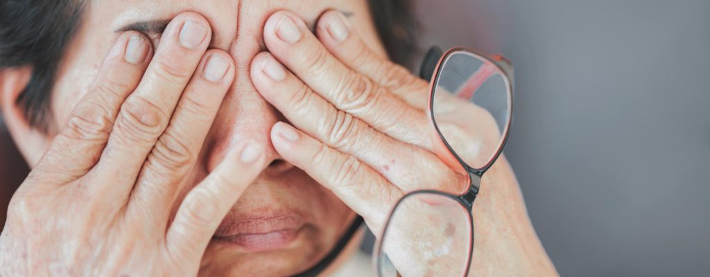 Mulher idosa aperta os olhos com as mãos por conta do desconforto causado pela DMRI.